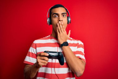 Yakışıklı afro-amerikan oyuncu video oyunu oynuyor... jostick ve kulaklıklar kullanıyor... ağzı ağızla kapatıyor... hata üstüne utanç, korku ifadesi, sessizlikten korkmak, gizli konsept.