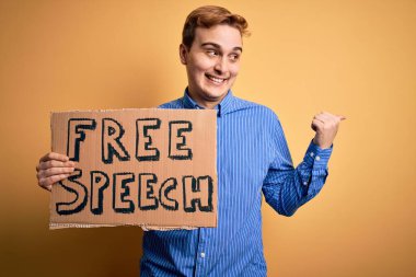 Genç, yakışıklı, kızıl saçlı, özgürlük isteyen özgür konuşma mesajı taşıyan pankartı tutan ve ağzı açık gülümseyen bir adam.