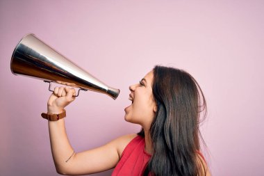 Genç, güzel, esmer kadın feryat ederek iletişim kuruyor. Pembe arka planda duran klasik bir megafon kullanıyor.