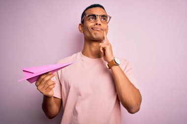 Genç, yakışıklı, Afro-Amerikalı bir adam pembe arka plan üzerinde kağıt uçak tutuyor.