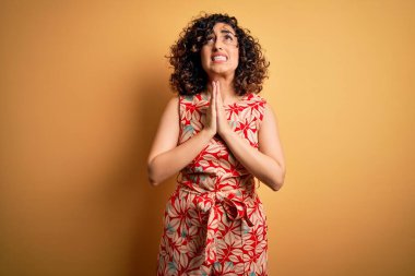 Genç ve güzel kıvırcık Arap kadın tatilde. Çiçekli bir elbise ve güneş gözlüğü takıyor. Elleri bağlı yalvarıyor ve dua ediyor. Yalvarıyorum..