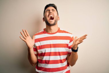 Sıradan çizgili tişört giyen genç yakışıklı adam izole edilmiş beyaz arka planda duruyor ve başarı için çılgın ve çılgın bir kutlama yapıyor kolları havada ve gözleri kapalı heyecanla bağırıyor. Kazanan konsept