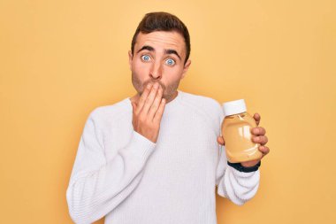 Genç, yakışıklı bir adam elinde hardal sosu şişesiyle sarı arkaplanı kapatıyor. Ağzını kapatıyor. Utanç verici bir hata, korku ifadesi, sessizlikten korkmak, gizli bir konsept.