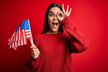 Amerika Birleşik Devletleri bayrağını kırmızı arka planda tutan güzel, vatansever kadın gülümsüyor.