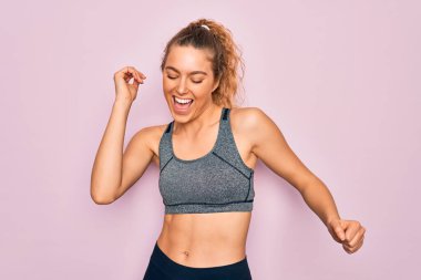 Mavi gözlü, genç, sarışın spor kadın spor kıyafetleri giyiyor mutlu ve neşeli dans ediyor, gülümsüyor rahat ve kendinden emin bir şekilde müzik dinliyor.