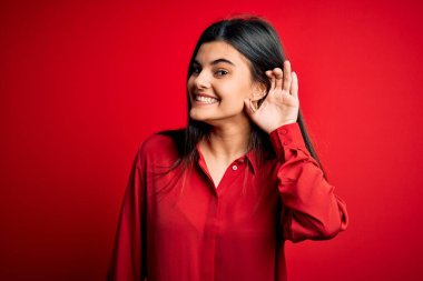 Genç, güzel, esmer bir kadın kırmızı arka planda dikilmiş dedikodu ve dedikodulara kulak misafiri olurken gülümsüyor. Sağırlık kavramı.