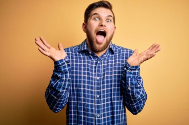 Sarışın, sakallı ve mavi gözlü genç bir işadamı sarı arka planda tişört giyip çılgınlığı kutluyor ve kollarını kaldırıp heyecanla haykırarak başarıyı kutluyor. Kazanan konsept