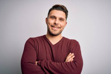 Mavi gözlü genç adam izole edilmiş arka planda dikilip kollarını kavuşturup kameraya bakarken gülümsüyor. Pozitif kişi.