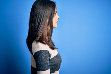 Mavi gözlü, sıradan çizgili tişörtler giyen genç esmer kadın arka planda duruyor. Yan tarafa bakıyor, rahat poz veriyor, kendine güvenen bir gülümsemesi var..