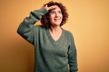 Orta yaşlı güzel kıvırcık saçlı kadın izole edilmiş sarı arka plan üzerine gündelik kazak giyiyor çok mutlu ve tebessüm ediyor. Konsept aranıyor.