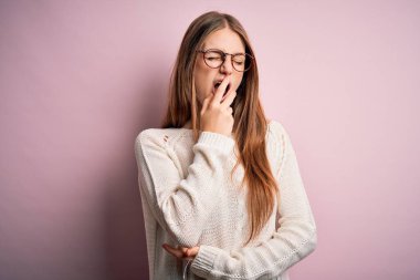 Genç, güzel, kızıl saçlı bir kadın pembe arka planda günlük süveter ve gözlük takıyor. Elle ağzını kapatmaktan sıkılmış. Huzursuz ve uykulu..
