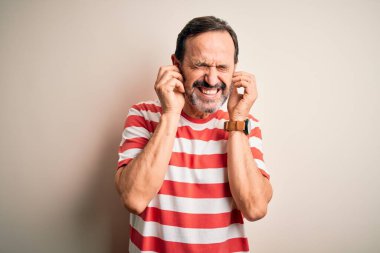 Orta yaşlı, beyaz tişörtlü bir adam izole edilmiş beyaz arka planda dikiliyor. Yüksek sesli müzik sesi için parmaklarıyla kulaklarını kapatıyor. Sağır kavramı.