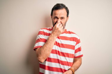 Orta yaşlı beyaz tişörtlü bir adam izole edilmiş beyaz arka planda dikiliyor pis ve iğrenç bir koku alıyor, nefesini burnunda tutuyor. Kötü kokuyor.