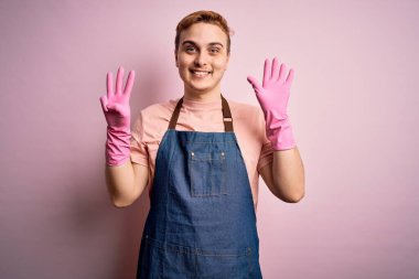 Genç, kızıl saçlı, önlük ve eldivenlerle ev işi yapan yakışıklı temizlikçi sekiz numarayı gösterip gösterirken kendinden emin ve mutlu bir şekilde gülümsüyor..