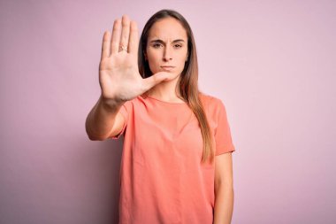 İzole edilmiş pembe arka plan üzerinde sıradan tişörtler giyen genç ve güzel bir kadın avuç içiyle şarkı söylemeyi kesiyor. Yüzünde olumsuz ve ciddi bir jest olan uyarı ifadesi.