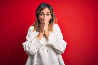 Orta yaşlı, güzel bir sporcu kadın izole edilmiş kırmızı arka planda günlük eşofman giyip gülüyor ve utanarak kıkırdıyor ağızları ellerle, dedikodularla ve skandallarla kaplıyor.