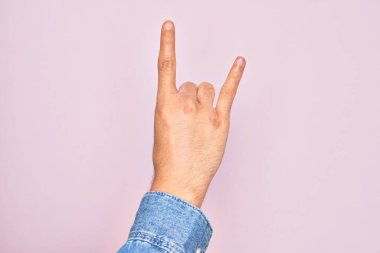 Kafkasyalı genç adam parmaklarını pembe arka planda gösteriyor rock 'n roll sembolü, müstehcen boynuzlar gösteriyor.