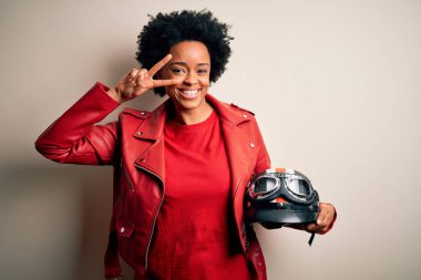 Kıvırcık saçlı motosiklet kasklı genç Afrikalı Afrikalı motosikletçi kadın. Barış sembolü yapıyor.