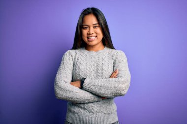 Genç, güzel Asyalı bir kız, sıradan bir süveter giyip mor arka planda duruyor. Kollarını kavuşturup kameraya bakarken gülümsüyor. Pozitif kişi.