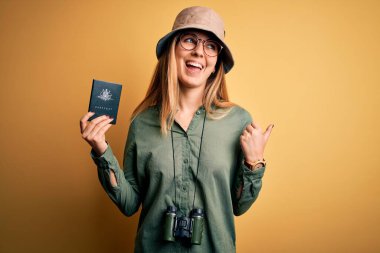 Sarışın, mavi gözlü, elinde Avustralya pasaportu olan bir turist. Dürbün kullanıyor ve gülümseyen bir yüzle baş parmağıyla gösteriyor.