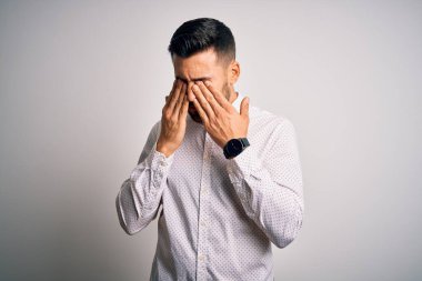 Soyutlanmış beyaz arka plan üzerinde duran zarif gömlek giyen genç yakışıklı adam yorgunluk ve baş ağrısı için gözlerini ovuşturuyor, uykulu ve yorgun ifade. Görüş sorunu