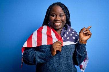 Genç vatansever Afro-Amerikan artı örgülü kadın. Birleşik Devletler bayrağı takıyor. Elleri ve parmakları kenarı işaret ederek çok mutlu.