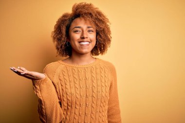 Kıvırcık saçlı, neşeli gülümseyen, avuç içi kameraya bakan güzel Afro-Amerikan kadın..
