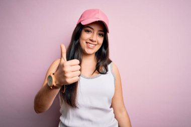 Pembe arka planda spor şapkası takan esmer genç bir kadın mutlu bir el hareketi yapıyor. Kameraya bakıp başarıyı gösteren ifade onaylanıyor.