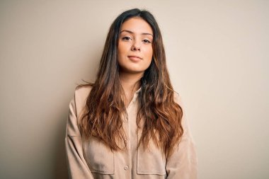 Genç, güzel esmer kadın, beyaz arka planda sıradan bir tişört giyiyor. Yüzünde ciddi bir ifadeyle rahatlamış. Basit ve doğal bir şekilde kameraya bakıyorsun..