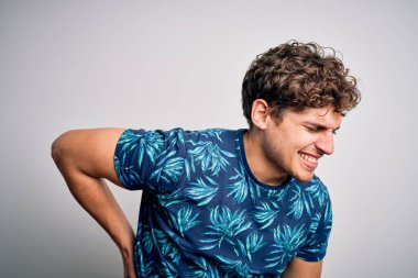 Sarışın, tatilde, kıvırcık saçlı, sıradan bir yaz tişörtü giyen sırt ağrısı çeken, elleriyle dokunarak karşılık veren, kaslı bir adam.