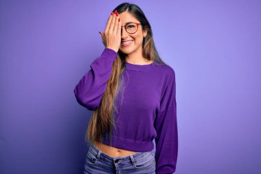 Genç, güzel, zeki bir kadın mor renkli gözlük takıyor. Bir gözünü elinle kapatıyor. Yüzünde kendine güvenen bir gülümseme ve sürpriz bir duygu var..