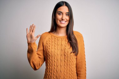 Genç, güzel esmer kadın izole edilmiş beyaz arka plan üzerine günlük süveter giyip beş numarayı gösterirken kendine güvenen ve mutlu bir şekilde gülümsüyor..