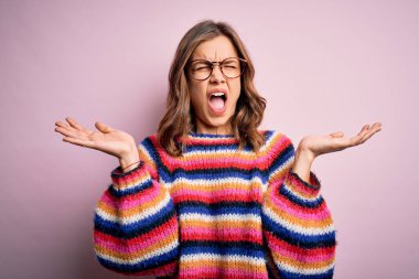 Genç, sarışın, gözlük takan ve pembe izole edilmiş arka planda rahat bir süveter giyen genç bir kız, çılgın ve başarıyı kollarını kaldırarak ve heyecanlı çığlıklar atarak kutluyor. Kazanan konsept