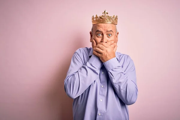 孤立したピンクの背景の上に王の黄金の冠を身に着けている中世の蜂蜜の男は間違いのための手で口をカバーショックを受けた 秘密概念 — ストック写真