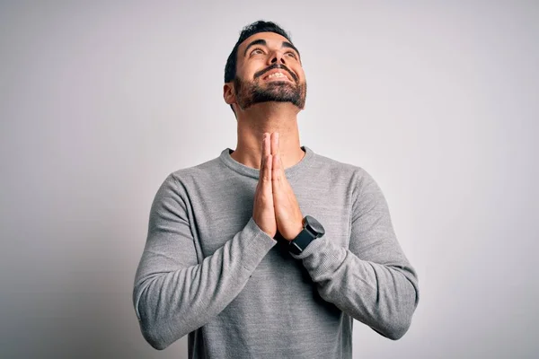 Young handsome man with beard wearing casual sweater standing over white background begging and praying with hands together with hope expression on face very emotional and worried. Begging.