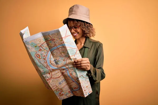 戴着探险家帽和水壶的非洲裔美国女游客拿着城市地图 脸上挂着快乐的表情 脸上挂着自信的微笑 露出牙齿 — 图库照片