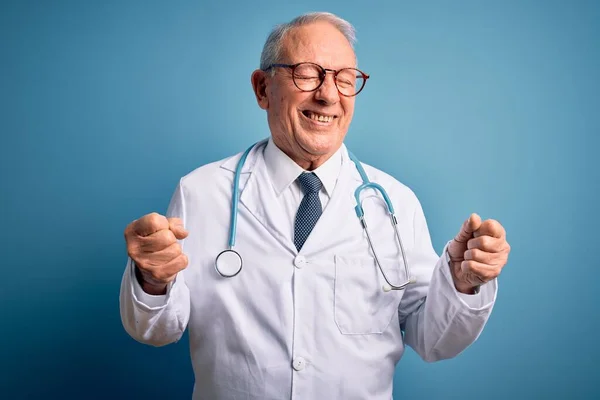 Starszy Siwowłosy Lekarz Noszący Stetoskop Płaszcz Medyczny Niebieskim Tle Podekscytowany — Zdjęcie stockowe