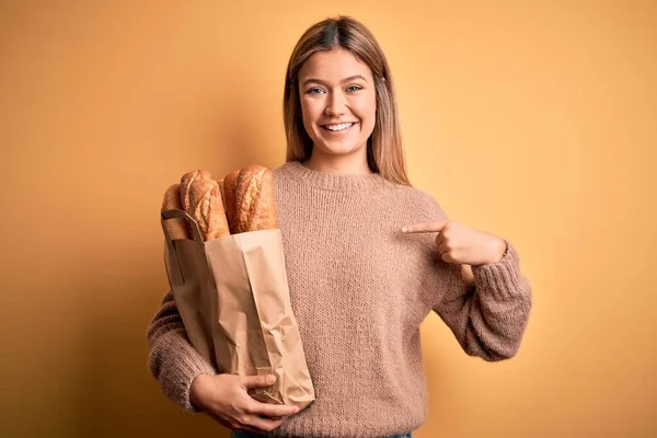 Молода Красива Жінка Тримає Паперовий Мішок Хлібом Над Ізольованим Жовтим — стокове фото