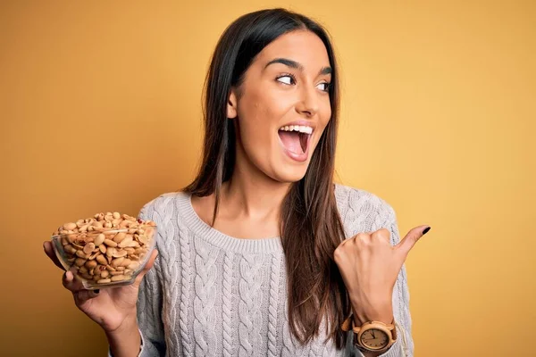 Joven Hermosa Morena Sosteniendo Tazón Con Cacahuetes Sobre Fondo Amarillo —  Fotos de Stock