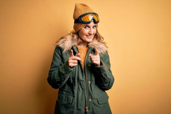 中年漂亮的金发滑雪者女人穿着雪地运动鞋和滑雪护目镜 手指指向镜头 脸上洋溢着欢乐和滑稽的表情 好的能量和活力 — 图库照片