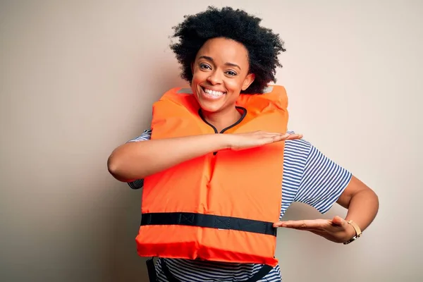 Young African American afro woman with curly hair wearing orange protection lifejacket gesturing with hands showing big and large size sign, measure symbol. Smiling looking at the camera. Measuring concept.