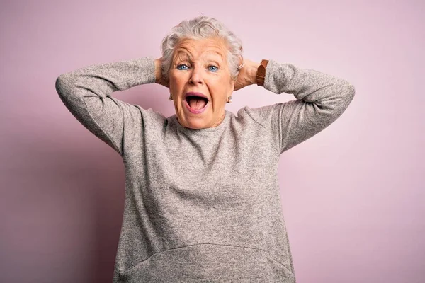 Senior beautiful woman wearing casual t-shirt standing over isolated pink background Crazy and scared with hands on head, afraid and surprised of shock with open mouth