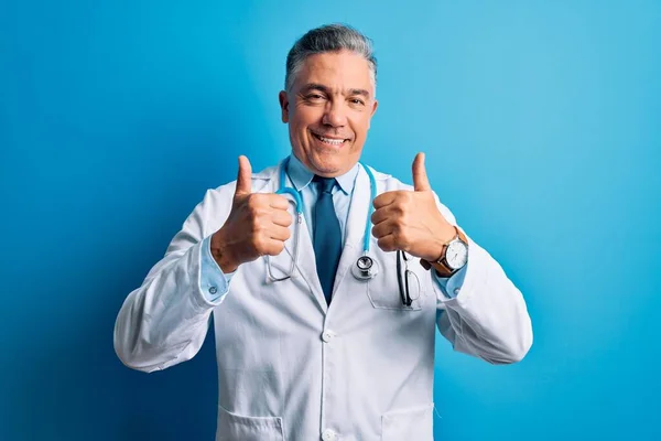 中年英俊 白发苍苍 身穿外套 头戴蓝色听诊器的医生成功地做了一个手势 用手做了一个积极的手势 竖起大拇指 微笑着 快乐地 快乐的表情和胜利的姿态 — 图库照片