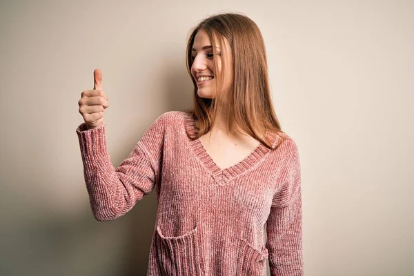 若いです美しいです赤毛女性身に着けていますピンクカジュアルなセーター上の隔離された白い背景誇りに思っています 笑顔やって親指アップジェスチャーへ側 — ストック写真