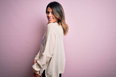 Moda kıyafetleri giyen genç ve güzel bir kadın. Manken, sokak tarzı giyiniyor. Pembe arka planda dikiliyor.