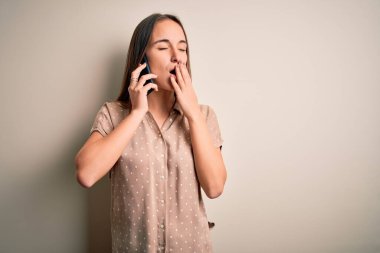 Genç ve güzel bir kadın beyaz arka planda akıllı telefondan konuşuyordu. Ağzı eliyle kapatmaktan sıkılmıştı. Huzursuz ve uykulu..