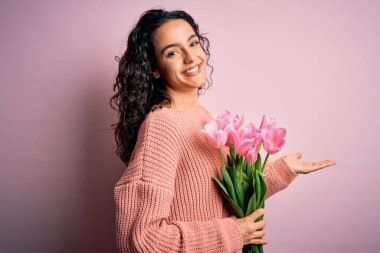 Güzel, kıvırcık saçlı, elinde pembe lale buketi olan genç, romantik bir kadın. Avuçları açık, fotokopi alanını gösteren, mutlu bir şekilde gülümseyen bir reklam sunan eller.