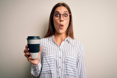 Genç, güzel esmer kadın beyaz arka planda bir fincan kahve içiyor. Şaşırmış bir yüzle korkmuş ve korku ifadesinden heyecanlanmış.