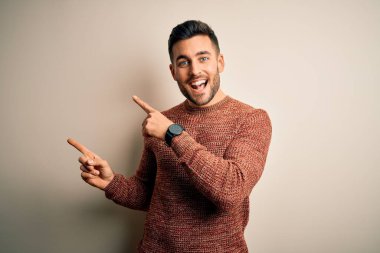 İzole edilmiş beyaz arka planda dikilip gülümseyen ve kamerayı iki eliyle ve parmaklarıyla gösteren genç, yakışıklı bir adam..