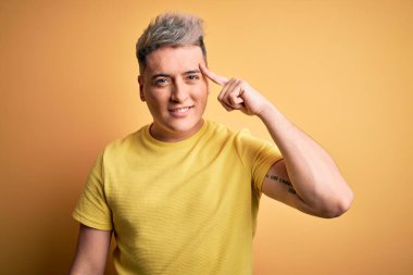 Sarı izole edilmiş arka plan üzerinde sarı tişört giyen genç, yakışıklı, modern bir adam. Tek parmağıyla gülümseyerek, harika bir fikir ya da düşünceyle, iyi bir hafızayla.